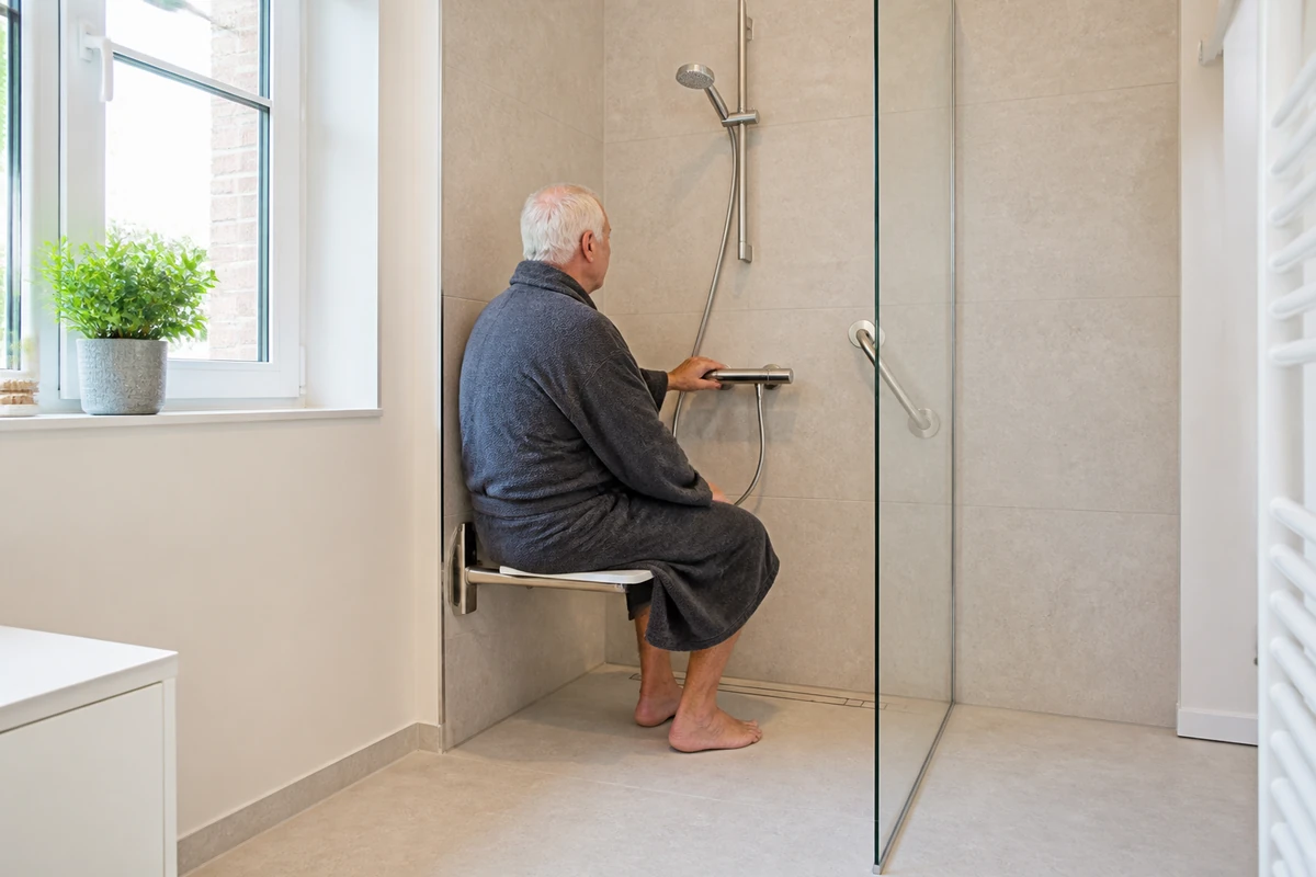 Personne assise dans une douche senior atteignant facilement le mitigeur placé à côté du siège